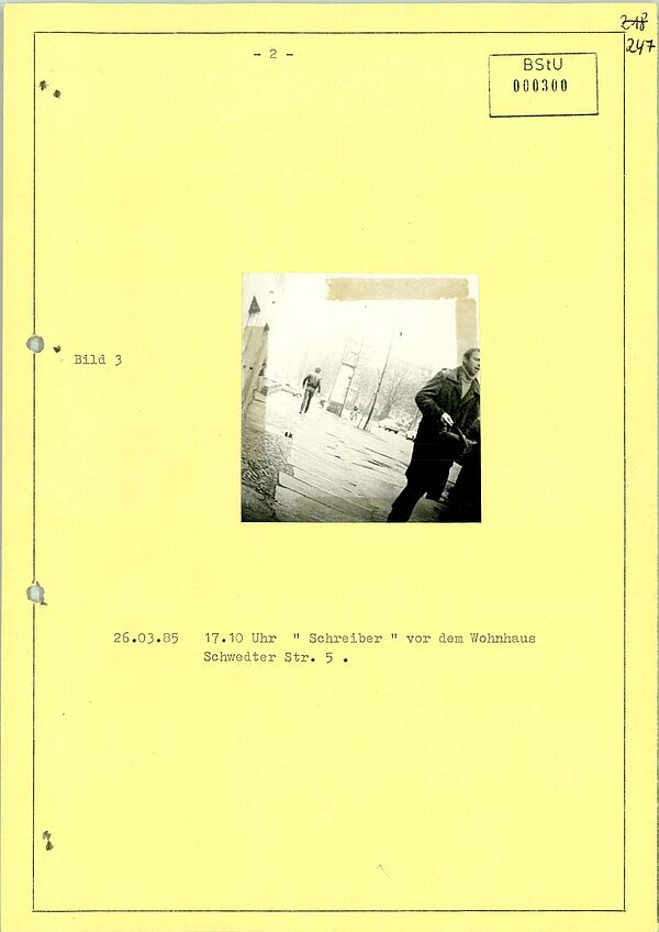 Ein auf einem gelben Blatt aufgeklebtes Foto mit Bildunterschrift. Am rechten Rand ist ein Mann, der in Richtung der Kamera läuft.