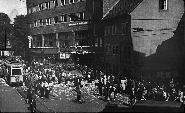 Schwarz-Weiß-Foto des gleichen Platzes. Zu sehen ist eine kleinere Menschenmenge, die einem Panzer umringt. Am rechten Rand ist eine Straßenbahn zu sehen.