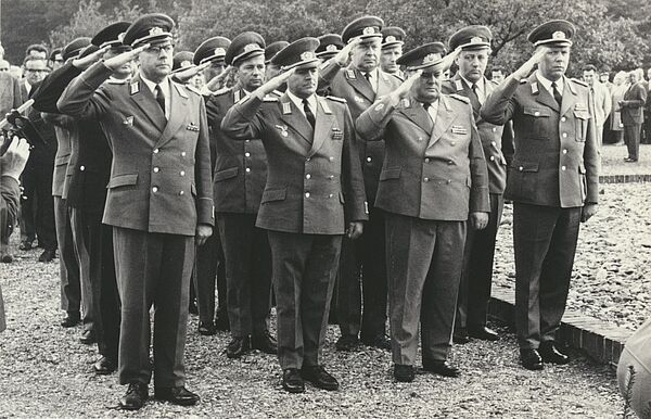 Das Foto ist mit der Thälmann Gedenktafel im Rücken aufgenommen. Die Offiziere sind davor angetreten und salutieren.
