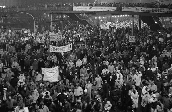 Eine große Menschenmenge auf einer Straße. Sie tragen verschiedene Transparente, auf einem steht "Streikrecht!". rechts ist eine Fußgängerbrücke, die ebenfalls voller Menschen ist. 