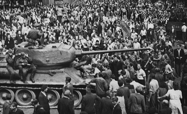 Schwarz-Weiß-Foto einer Menschenmenge, die einen Panzer umringt, auf dem bewaffnete Soldaten sitzen.