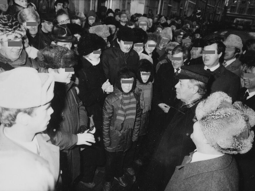 Helmut Schmidt und Erich Honecker auf dem Weihnachtsmarkt in Güstrow bei einem inszeniert erscheinenden Gespräch mit einer Familie mit zwei Kindern. Sie sind von Schaulustigen umringt. Alle wirken locker und freundlich.