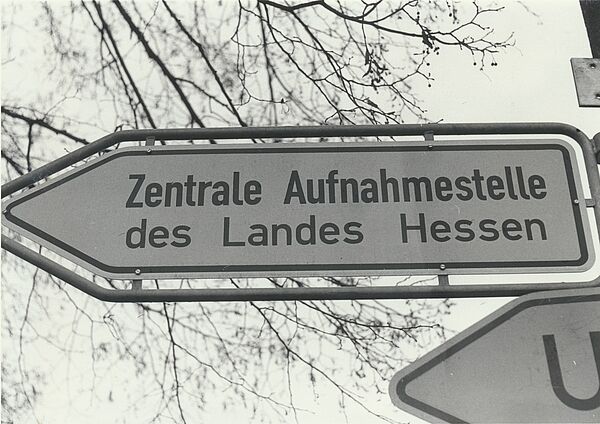 Schwarz-Weiß-Foto eines nach Links zeigendes Verkehrsschilds mit der Aufschrift "Zentrale Aufnahmestelle des Landes Hessen".
