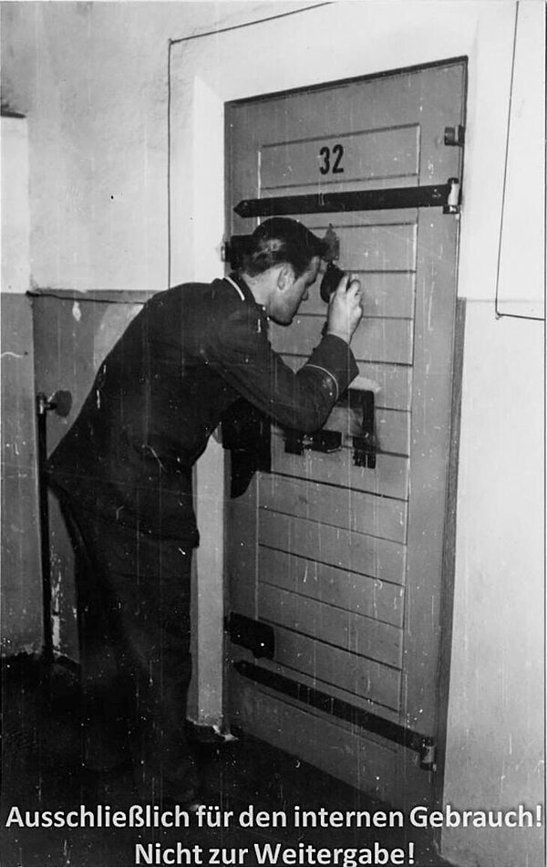 Schwarz-Weiß-Foto eines unifmorieten Mannes, der durch einen Schlüsselspion in eine Zellentür schaut.
