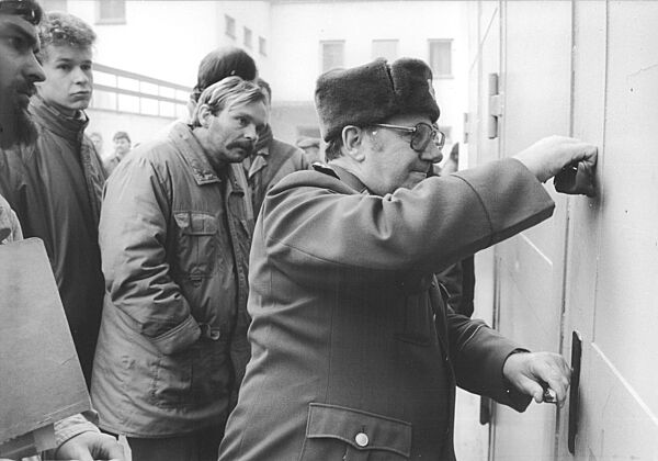 Ein Mann in militärischer Uniform versiegelt eine Tür. Hinter ihm stehen Personen, die interessiert zuschauen.