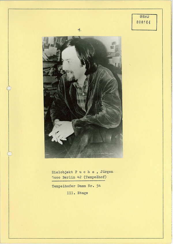 Auf einer Seite aufgeklebtes Schwarz-Weiß-Foto auf dem ein lachender Mann mit längeren Haaren und Bart zu sehen ist. Darunter stehen mit Schreibmaschine geschriebene biografische Daten.