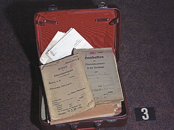 Blick auf den geöffneten Roten Koffer, in dem unordentlich Unterlagen liegen.