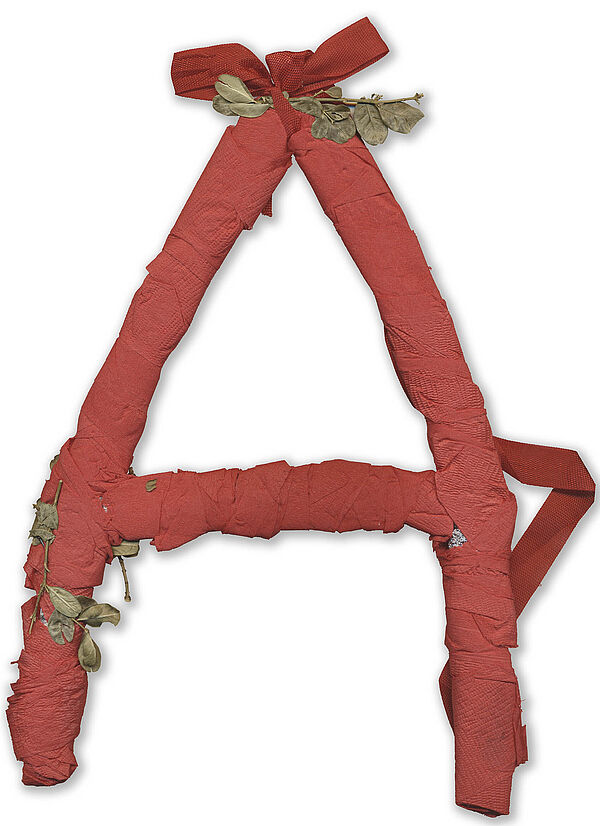 Ein aus rotem Krepppapier gebasteltes "A", verziert mit getrockneten Blättern.