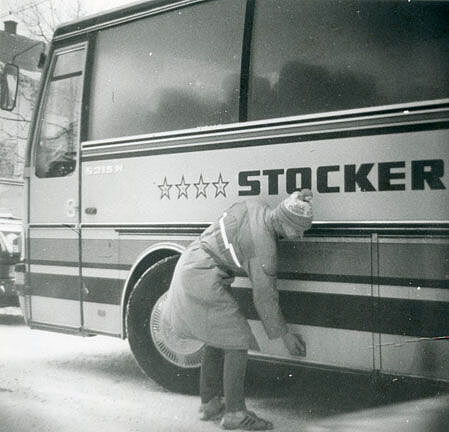 Ein Mann in Winterkleidung öffnet mit nach unten gebeugtem Oberkörper den Gepäckraum eines Reisebusses.