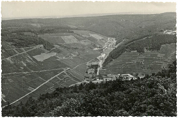 Luftbild mit dem Blick in ein Tal in einer hügeligen Landschaft. Im Tal sind Straßen und Gebäude zu erkennen.