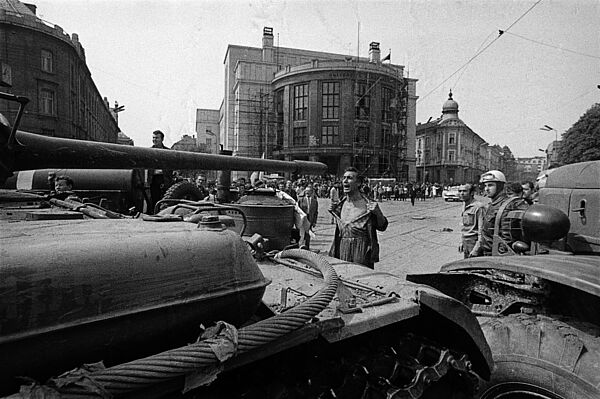 Ein Mann mit entblößtem Oberkörper steht vor einem Panzer und schreit, in das Kanonenrohr blickend, etwas.