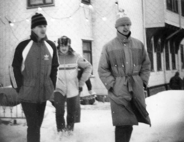 Drei Männer in Winterkleidung spazieren durch eine winterlich verschneite Ortschaft.