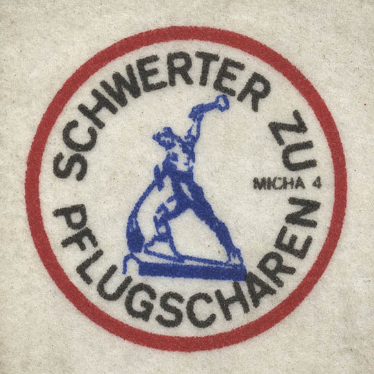 Das Bild zeigt ein Foto eines Aufnähers mit der Aufschrift "Schwerter zu Pflugscharen" und ein Abbild der gleichnamigen Skulptur