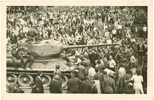 Schwarz-Weiß-Foto einer Menschenmenge, die einen Panzer umringt, auf dem bewaffnete Soldaten sitzen.