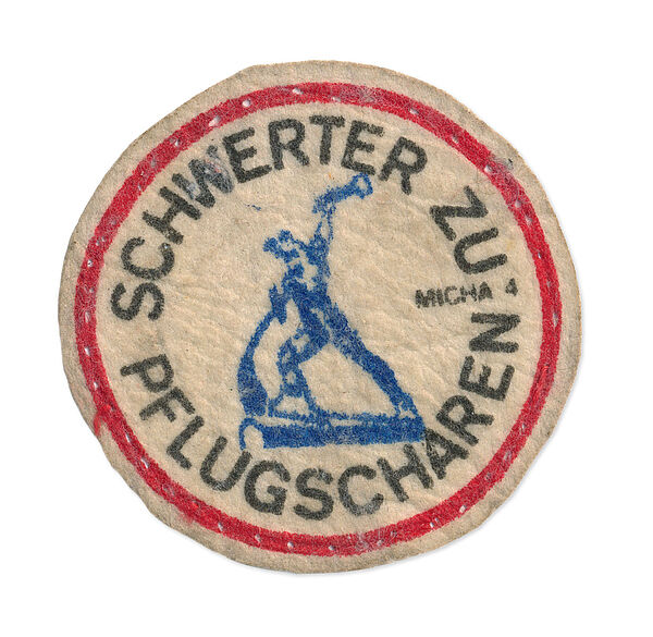 Aufnäher mit der Losung "Schwerter zu Pflugscharen", Quelle: BArch, MfS, BV Leipzig, KD Döbeln, Nr. 483, Bl. 1 Das Bild zeigt einen Aufnäher mit der schwarzen kreisförmigen Aufschrift "Schwerter zu Pflugscharen" umrahmt mit einem roten Kreis, darin in blau ein Abbild der gleichnamigen Skulptur