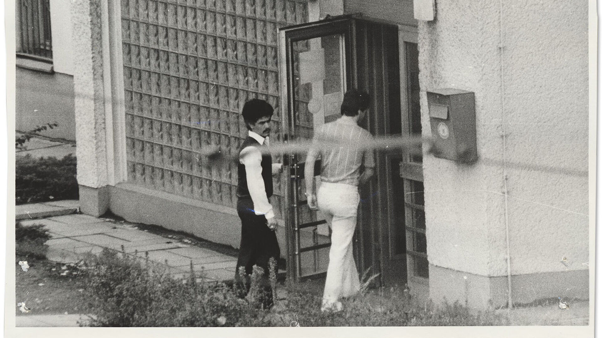 Stasi-Observationsfoto: Einer der Männer (links), die an dem Attentat auf die West-Berliner Diskothek "La Belle" beteiligt waren, beim Betreten der libyschen Botschaft in Ost-Berlin, Juni 1986 Schwarz-Weiß-Foto zweier Männer, die ein Gebäude betreten.