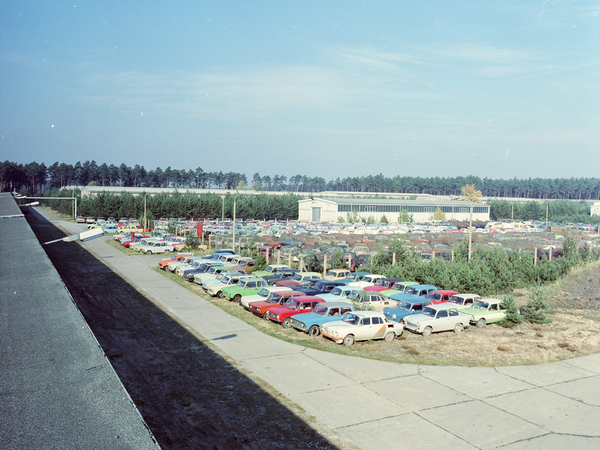 Blick von einem Lagerhallendach über eine weite Fläche voller KFZ mit unterschiedlichen Farben. Im Hintergrund Lagergebäude.