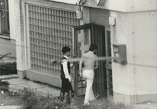 Anscheinend unbemerkt gemachtes Schwarz-Weiß-Foto zweier Männer, die ein Gebäude betreten.