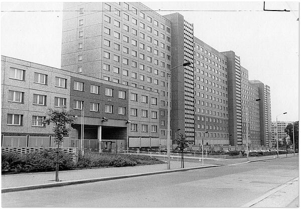 "Haus 16" (Bildmitte) in der Stasi-Zentrale in Berlin-Lichtenberg: Dienstsitz der HA XVIII; Quelle: BArch, MfS, BdL, Fo, Nr. 295, Bild 7 Schwarz-Weiß-Foto eines mehrgeschössigen Plattenbaus. Im Vordergrund ist eine nicht befahrene Straße.