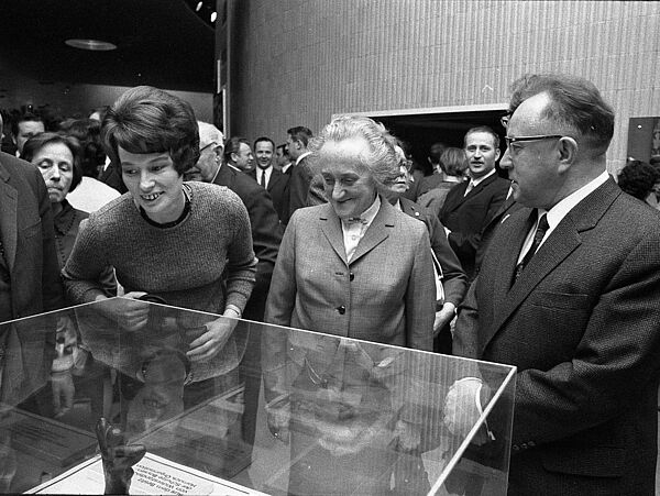 Im Foyer des Kinos Kosmos in Ost-Berlin stehen Kuckhoff, Adolphi und Mielke vor einer halbhohen Vitrine und unterhalten sich.