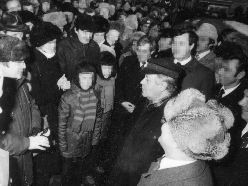 Helmut Schmidt und Erich Honecker auf dem Weihnachtsmarkt in Güstrow bei einem inszeniert erscheinenden Gespräch mit einer Familie mit zwei Kindern. Sie sind von Schaulustigen umringt. Alle wirken locker und freundlich.