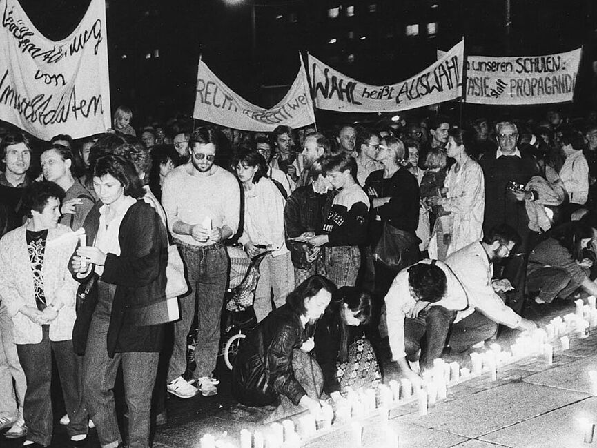 Foto einer Demonstration. Die Menschen vorne stellen brennende Kerzen ab. Hinter ihnen sieht man Hochtransparente.