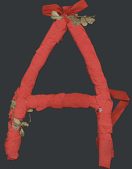 Ein aus rotem Krepppapier gebasteltes "A", verziert mit getrockneten Blättern.