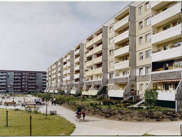 Blick auf einen neuen Plattenbau-Block in der rechten Bildhälfte. Links davor eine Grünfläche. Im Hintergrund ein weiterer Plattenbauriegel.