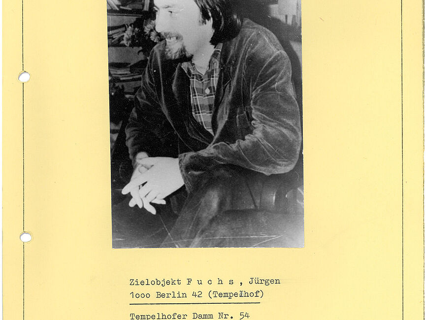 Auf einer Seite aufgeklebtes Schwarz-Weiß-Foto auf dem ein lachender Mann mit längeren Haaren und Bart zu sehen ist. Darunter stehen mit Schreibmaschine geschriebene biografische Daten.