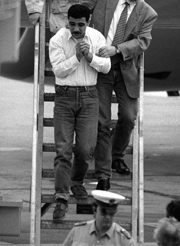 Ein mit Handschellen gefesselter Mann wird eine schmale Flugzeug-Gangway hinab geführt.