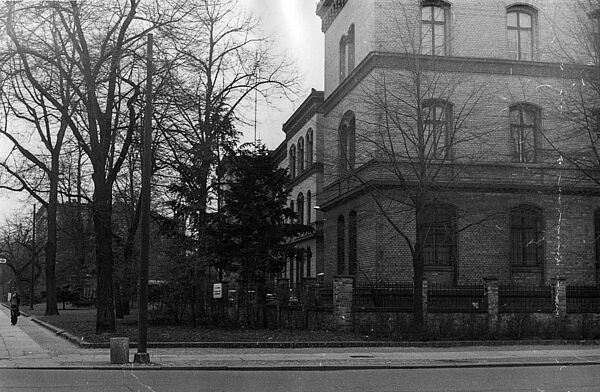 Stasi-Verwaltung Groß-Berlin (ab 1977 BV Berlin), Prenzlauer Allee 63–67 Das Bild ist über eine Straße fotografiert. Es zeigt ein Fabrikgebäude aus der Gründerzeit. Die Wandflächen bestehen aus beigen Ziegeln, Gesimse aus rot-braunen Ziegelelementen. Davor stehen Bäume ohne Laub.