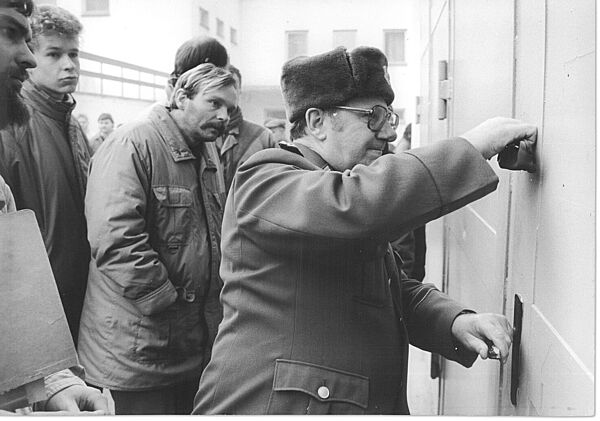 Ein Mann in militärischer Uniform versiegelt eine Tür. Hinter ihm stehen Personen, die interessiert zuschauen.