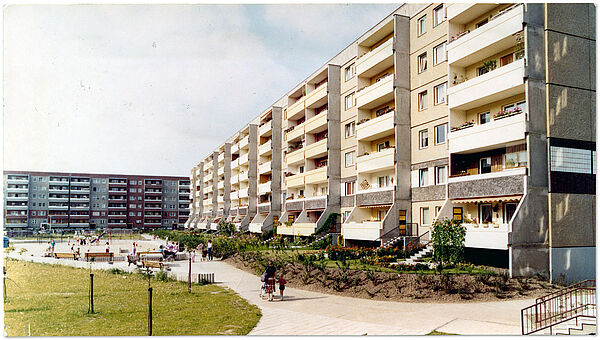 Blick auf einen neuen Plattenbau-Block in der rechten Bildhälfte. Links davor eine Grünfläche. Im Hintergrund ein weiterer Plattenbauriegel.