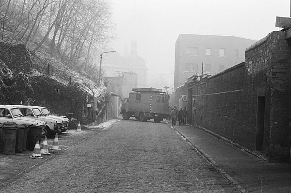 Foto einer Straße, die von einem Lastwagen blockiert wird. Rechts ist eine dicke Mauer zu sehen, links ein Hügel, der nach oben ansteigt..