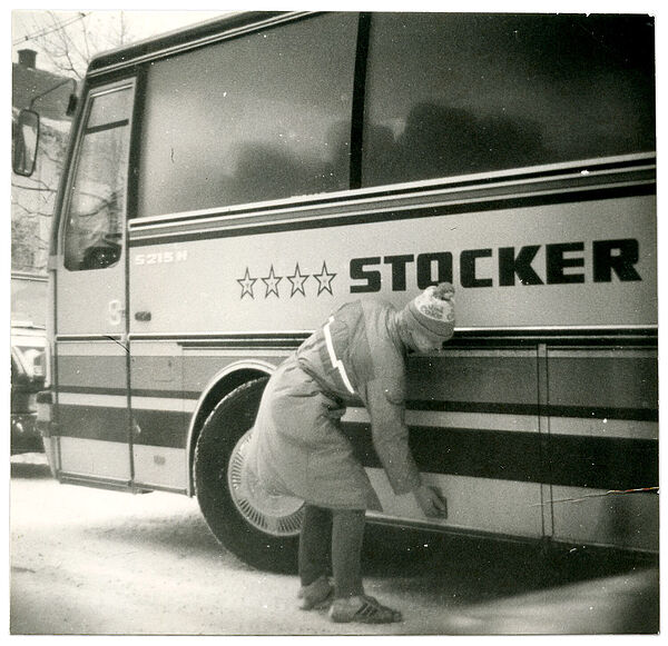 Ein Mann in Winterkleidung öffnet mit nach unten gebeugtem Oberkörper den Gepäckraum eines Reisebusses.
