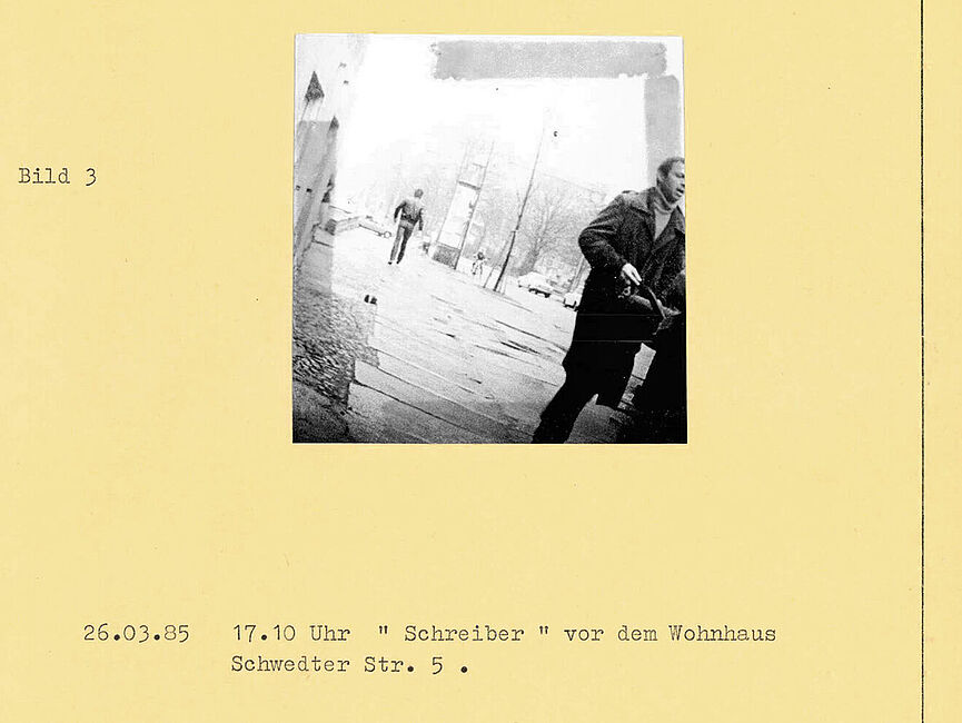 Bildbericht der Observation Radulovics durch Mitarbeiter der HA VIII am 26. März 1985 Ein auf einem gelben Blatt aufgeklebtes Foto mit Bildunterschrift. Am rechten Rand ist ein Mann, der in Richtung der Kamera läuft.