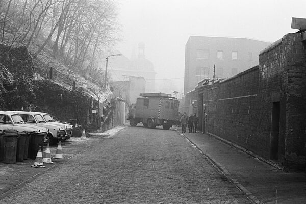 Foto einer Straße, die von einem Lastwagen blockiert wird. Rechts ist eine dicke Mauer zu sehen, links ein Hügel, der nach oben ansteigt..