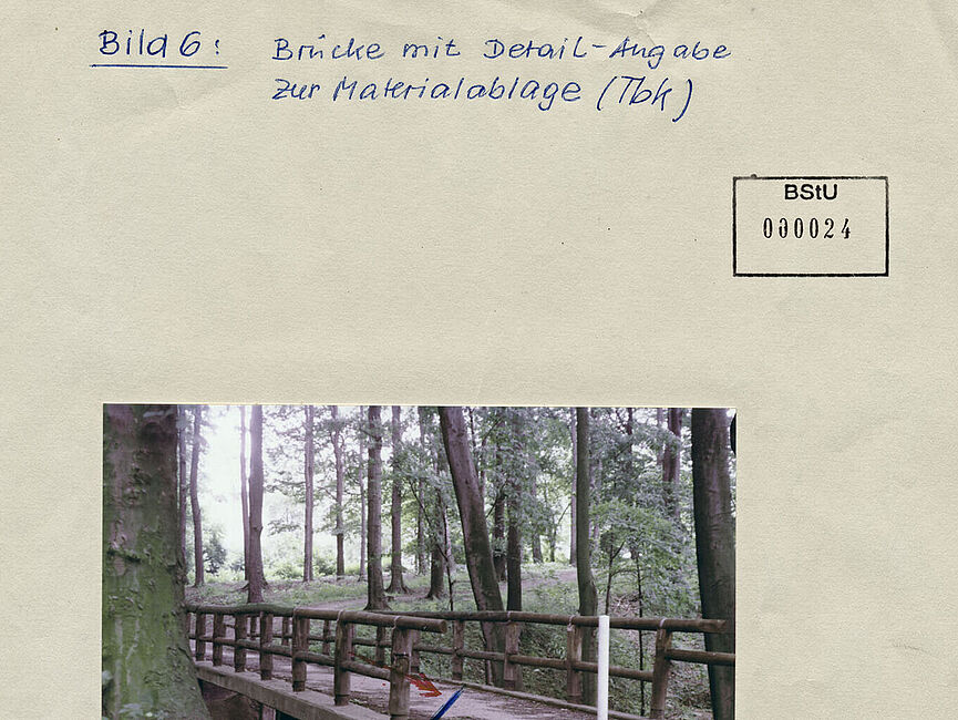 Stasi-Bildbericht zum TBK "Brücke" im Essener Lührmannwald, November 1985 Foto der Brücke im Waldgebiet Lührmannwald in Essen, unter der sich der Tote Briefkasten befindet. Ein Pfeil weist dessen Position aus.