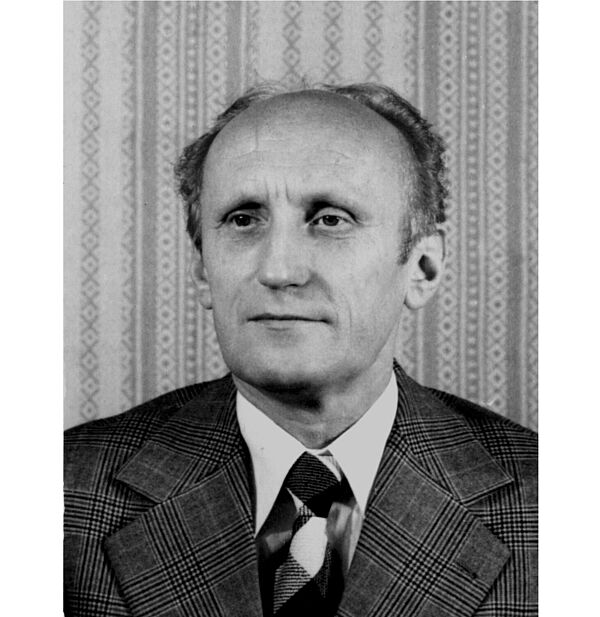 Schwarz-Weiß-Foto, auf dem Oberkörper und Gesicht eines älteren Mannes mit Halbglatze mit kariertem Jacket und Krawatte vor einer gemusterten Tapete zu sehen ist.