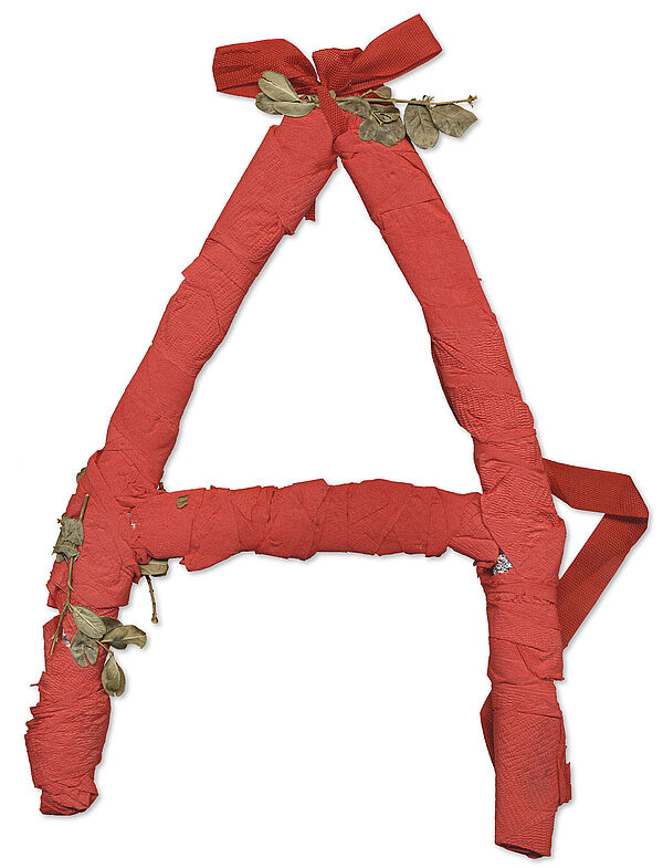 Ein aus rotem Krepppapier gebasteltes "A", verziert mit getrockneten Blättern.