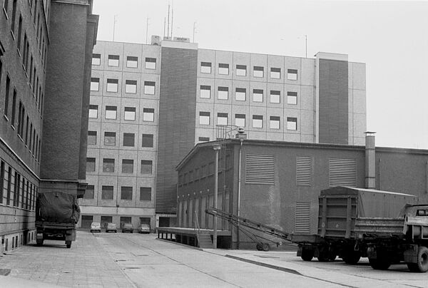 Blick über einen schmalen Hof ein siebengeschossiges Neubaugebäude aus den 1980er-Jahren.