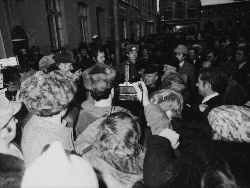 Helmut Schmidt und Erich Honecker auf dem Weihnachtsmarkt in Güstrow, umringt von einer Menschenmenge. Fotografen halten Kameras hoch, um ein Bild von der Szene zu machen.