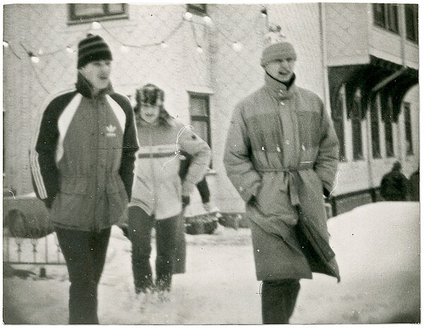 Drei Männer in Winterkleidung spazieren durch eine winterlich verschneite Ortschaft.