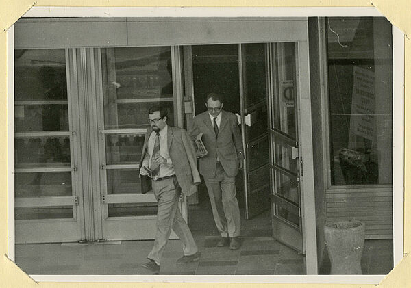 Beobachtungsfoto vom Eingang des Interhotels "Unter den Linden" in Ost-Berlin, 1974; Quelle: BArch, MfS, HA VIII, Fo, Nr. 330, Bl. 10 (Ausschnitt) Schwarz-weiß-Foto zweier anzugtragender Männer, die den Eingangsbereich eines Gebäudes verlassen.