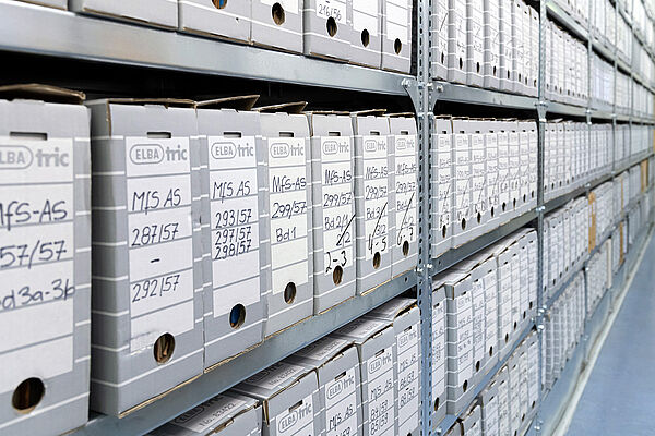 Zu sehen sind Schwerlastregale, die mit zahlreichen Pappboxen gefüllt sind, in denen Papier zu sehen ist. Beschriftet sind sie mit "MfS AS" und ansteigenden Nummern.
