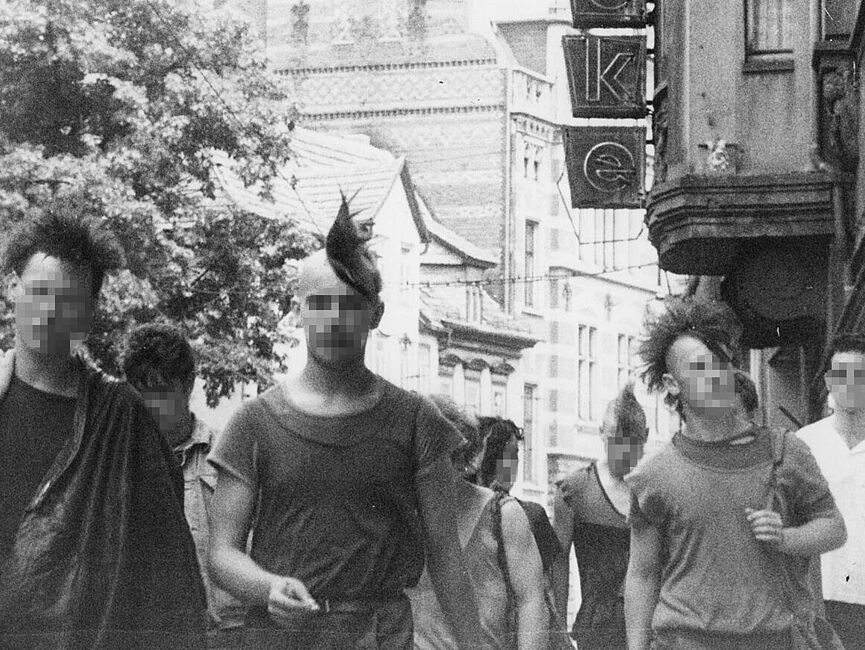 Schwarz-Weiß-Foto einer Gruppe Jugendlicher im Punk-Look, im Hintergrund Häuser und Bäume.