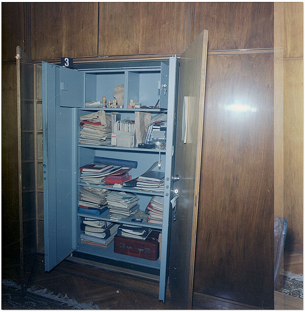 Blick auf einen mannshohen, in eine Schrankwand eingebauten Panzerschrank, in dem unordentlich anmutende Unterlagen liegen.