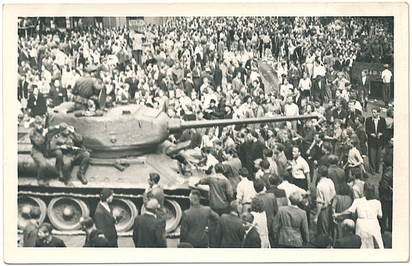 Schwarz-Weiß-Foto einer Menschenmenge, die einen Panzer umringt, auf dem bewaffnete Soldaten sitzen.