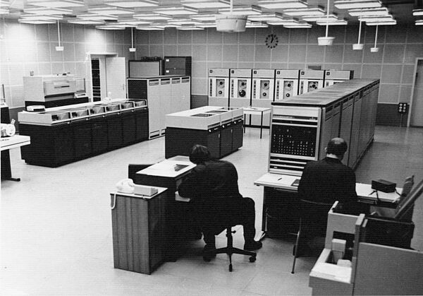 Computerraum im Zentralen Rechenzentrum Wuhlheide, 70er Jahre Foto einer Großrechneranlage aus den 1960er-Jahren mit Rechner-, Magnetband und Druckermodulen sowie zwei Operateuren an ihren Arbeitsplätzen.