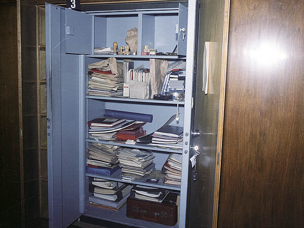 Blick auf einen mannshohen, in eine Schrankwand eingebauten Panzerschrank, in dem unordentlich anmutende Unterlagen liegen.